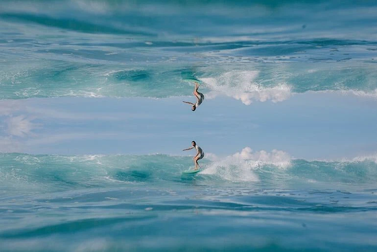 Horizontal mirror image effect on photo of man surfing small wave on blue surfboard made with photo editor