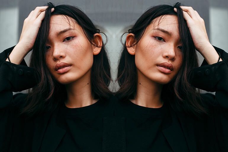 Mirror image effect on photo of woman in black shirt running hands through hair made with photo editor