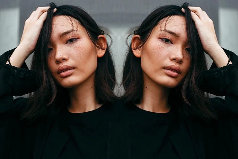 Mirror image effect on photo of woman in black shirt running hands through hair made with photo editor