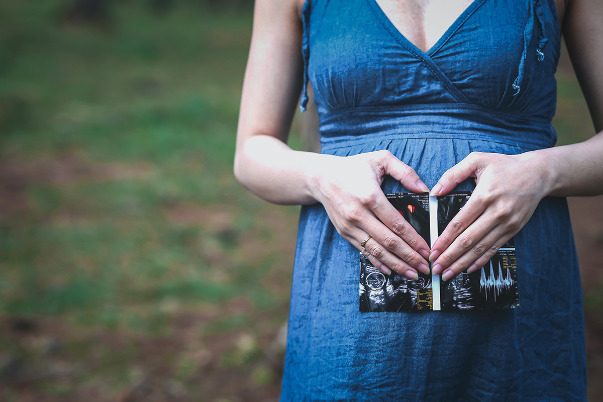 pregnant woman holding ultrasound photo with hands in heart shape