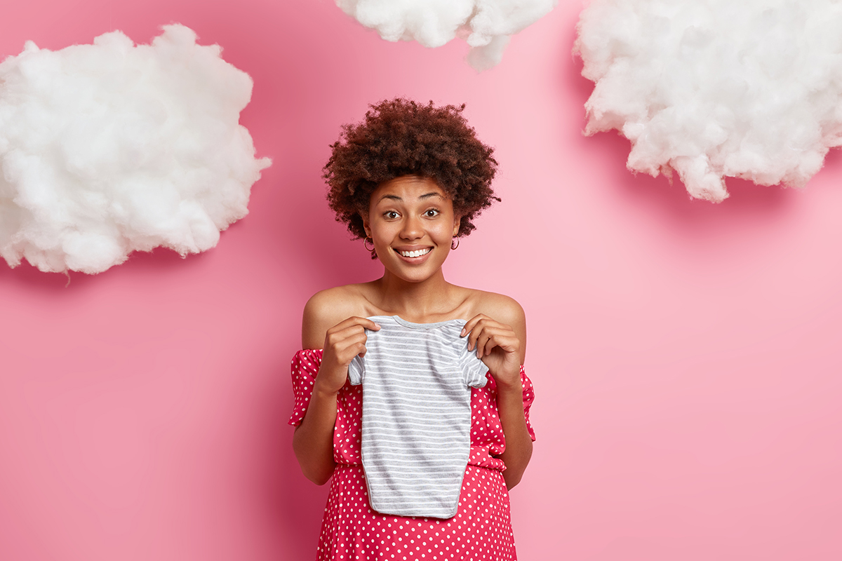 pregnant woman holding baby onesie on a pink background