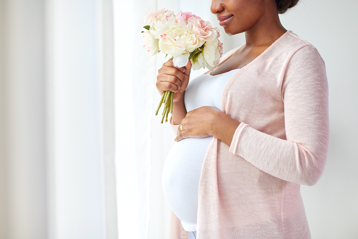 pregnant woman holding bouquet of flowers while touching her stomach for maternity photoshoot ideas