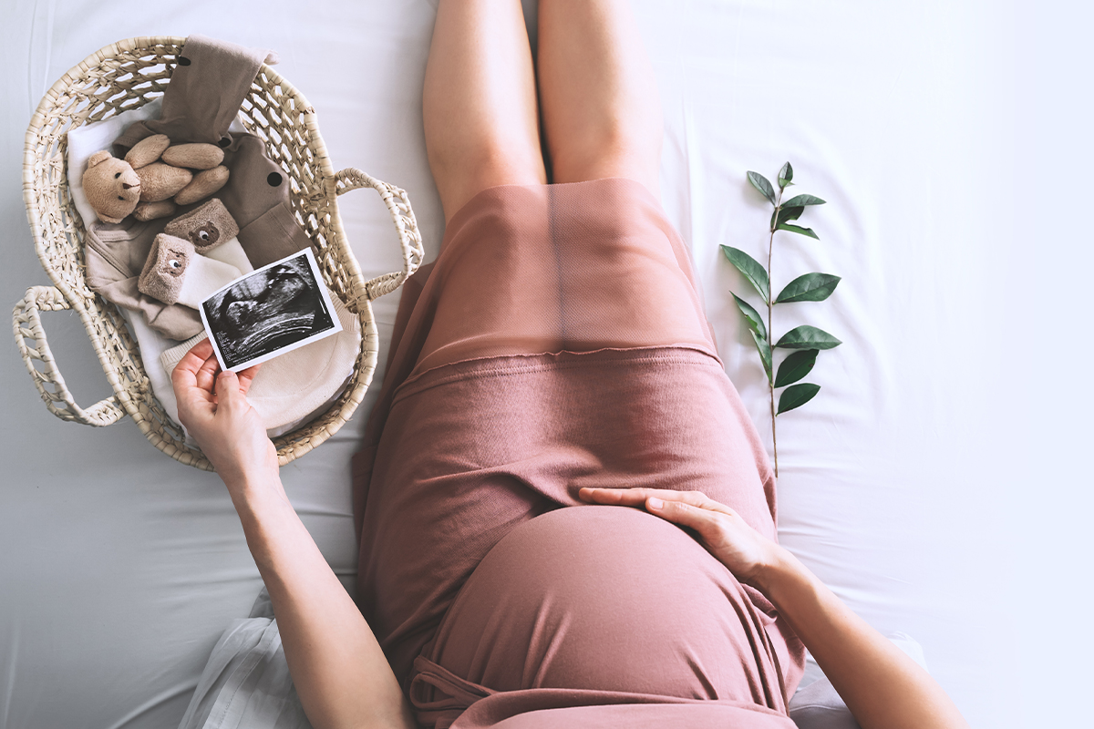 overhead shot of pregnant woman holding ultrasound photo with teddy bear in a basket