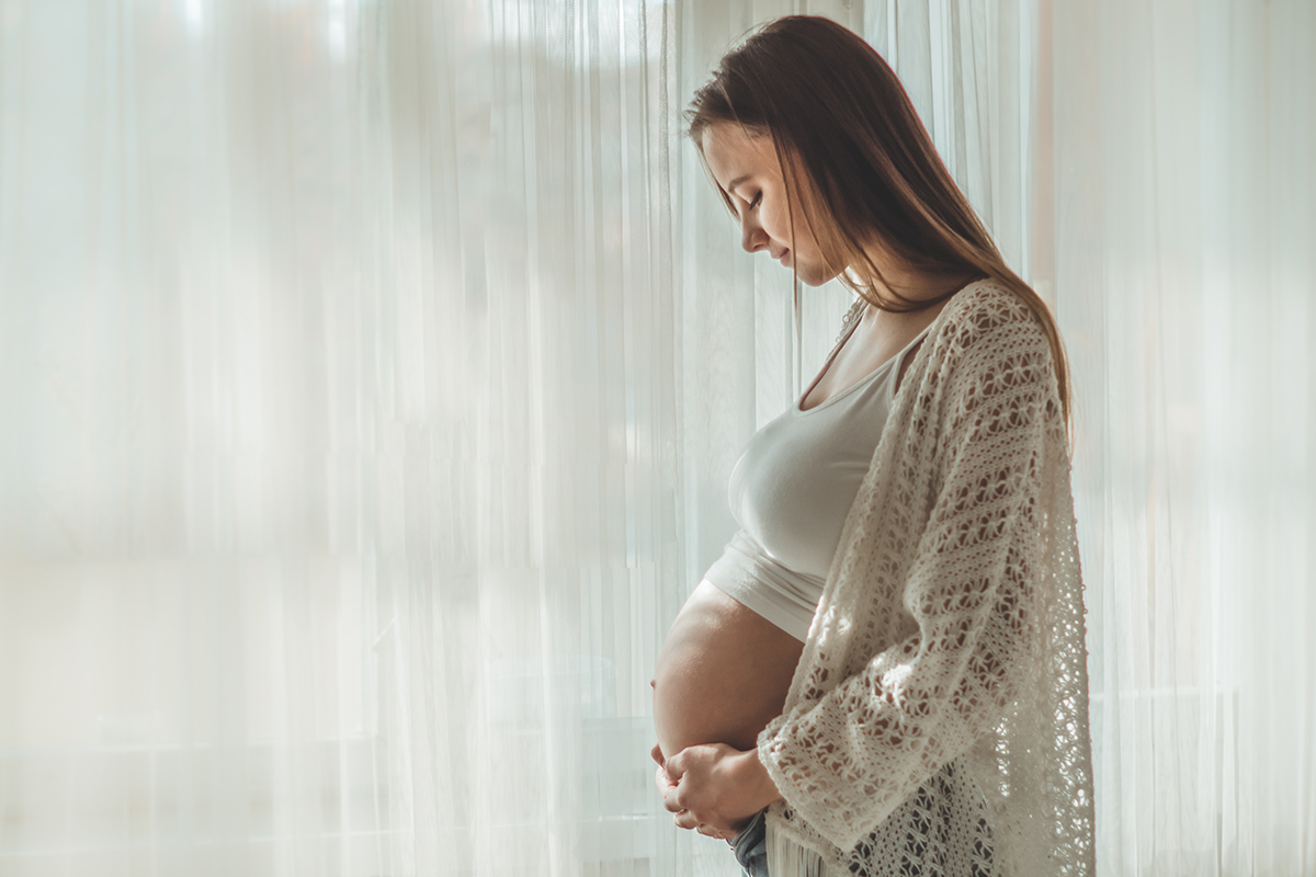 pregnant woman holding belly at golden hour by a window