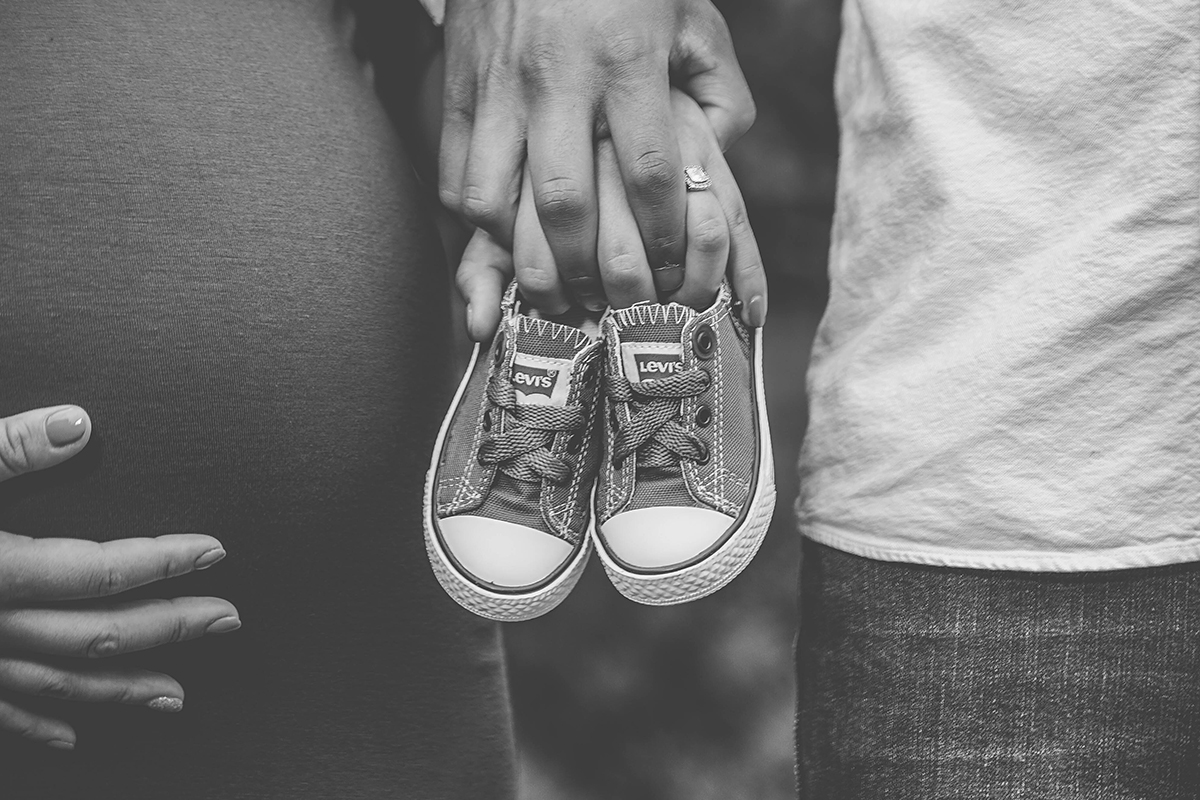 maternity photo ideas with a black and white filter and hands holding baby sneakers