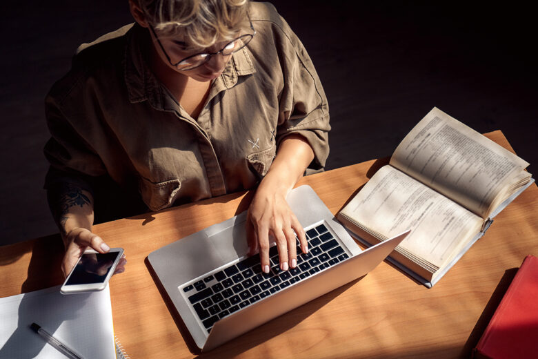 person sitting at desk in front of laptop with phone in hand